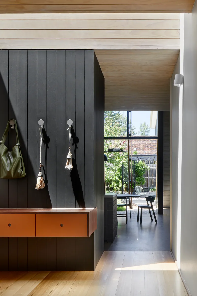 Entry hallway with charcoal-panelled wall and timber bench beneath wall-mounted hooks holding bags