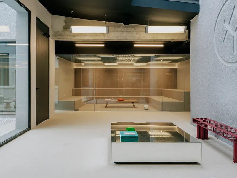 Interior gallery space with exposed concrete beams, black ceiling, glass vitrine, and views to courtyard beyond