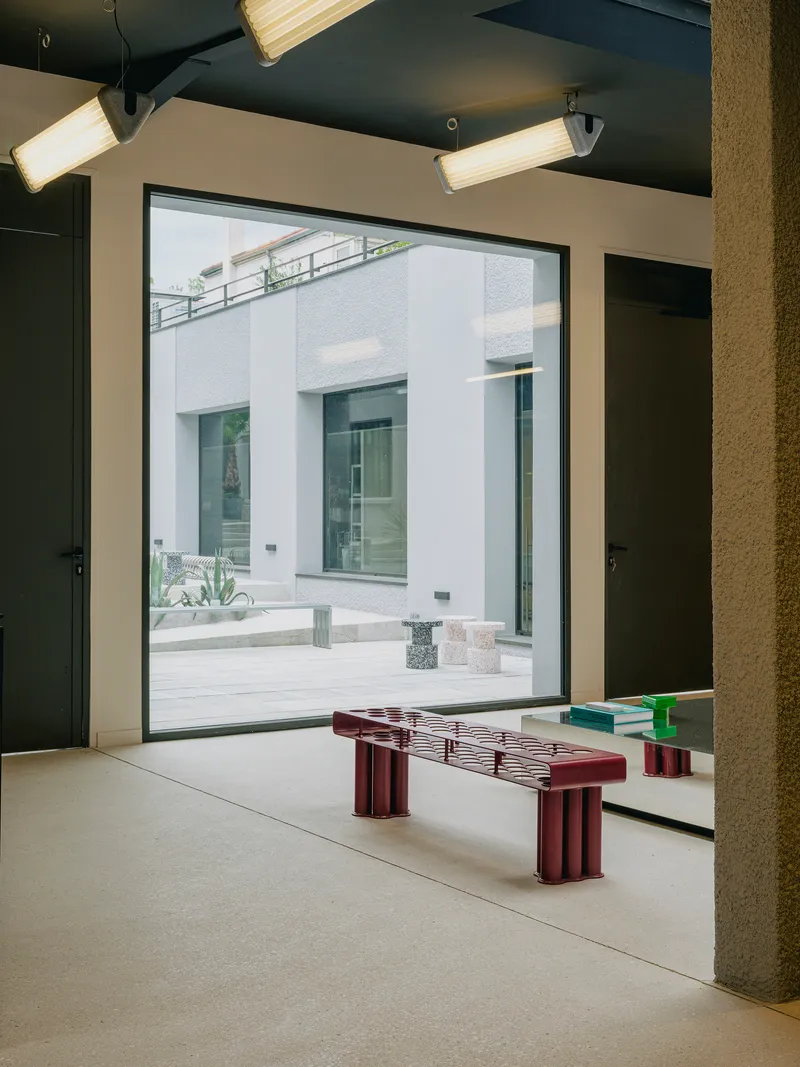 Interior room framing courtyard through full-height glazing with maroon slatted bench in foreground