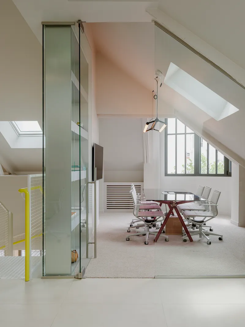 Attic meeting room with sloped ceilings, skylights, and glass partition separating workspace below