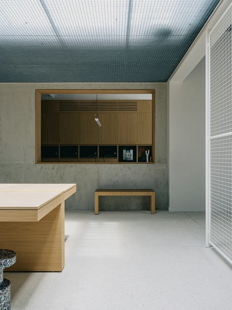Interior space with mesh ceiling, concrete walls, timber-lined service window, and white mesh partition