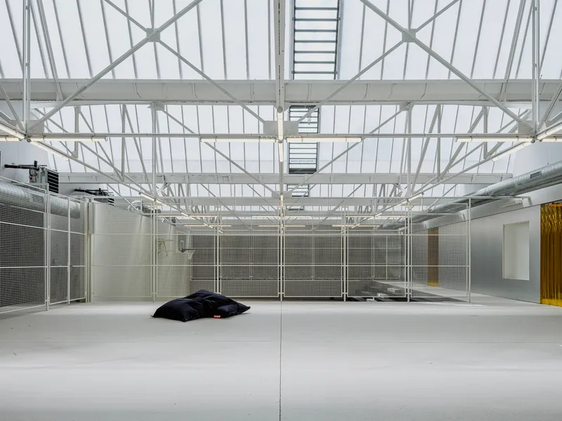 Large hall with white painted steel roof trusses, skylights, mesh partitions, and polished resin floor