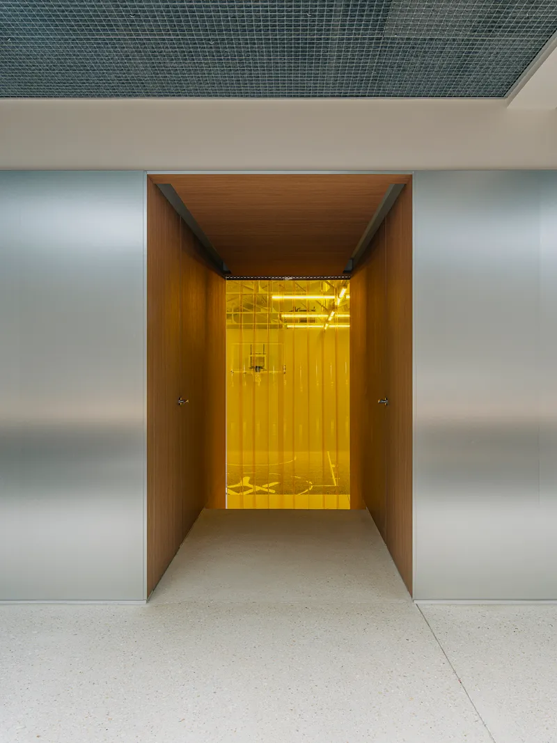 Wood-lined corridor leading to a yellow-lit elevator vestibule framed by brushed metal walls
