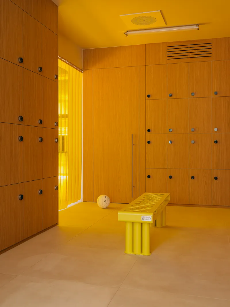 Locker room with yellow walls and ceiling, timber lockers with metal hardware, and yellow bench