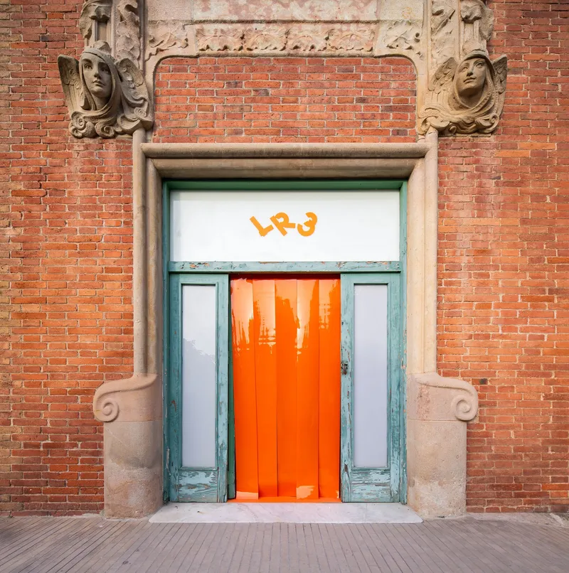 Ornate brick facade entrance with carved stone surround and orange vertical slats behind glass doors