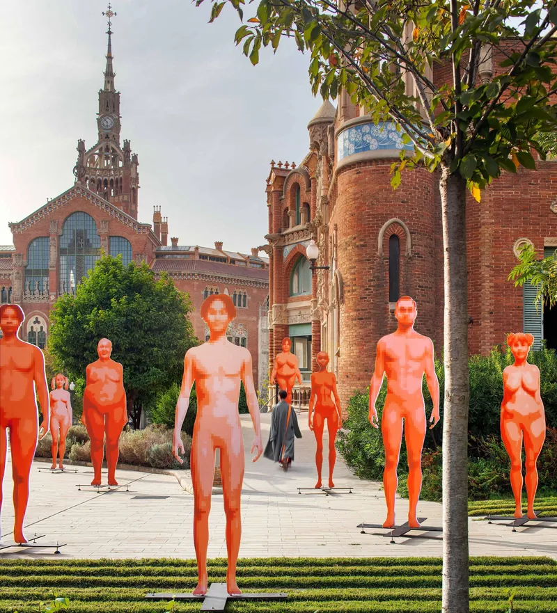 Outdoor plaza with orange sculptural figures among trees and historic brick tower in the background