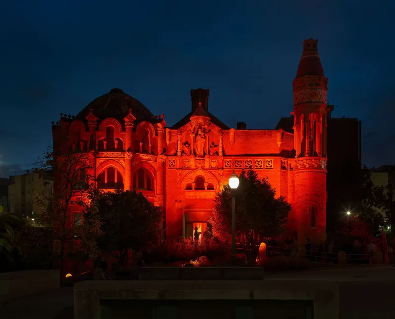 Historic brick building illuminated in red light at dusk with clock tower and arched entrance visible