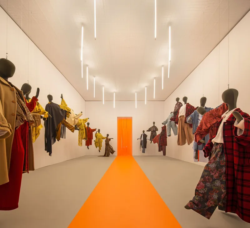Long view of the exhibition hall with wall-mounted textile displays and vertical tube lighting in the ceiling