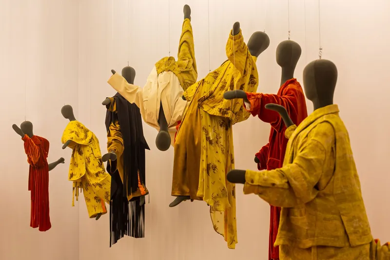 Close-up of clustered mannequins draped in yellow and red fabrics suspended from ceiling wires