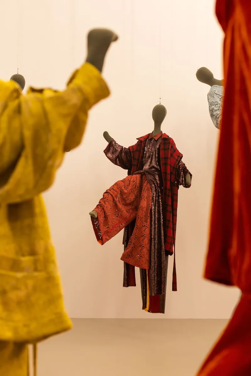 Detail of a single mannequin wearing layered plaid and patterned textiles against a white wall
