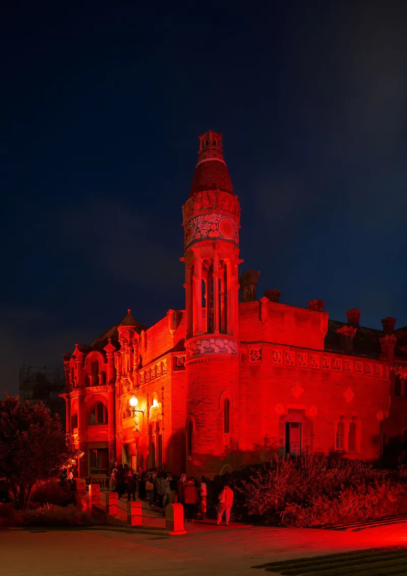Ornate tower with carved detailing illuminated in red light at night with visitors gathered below
