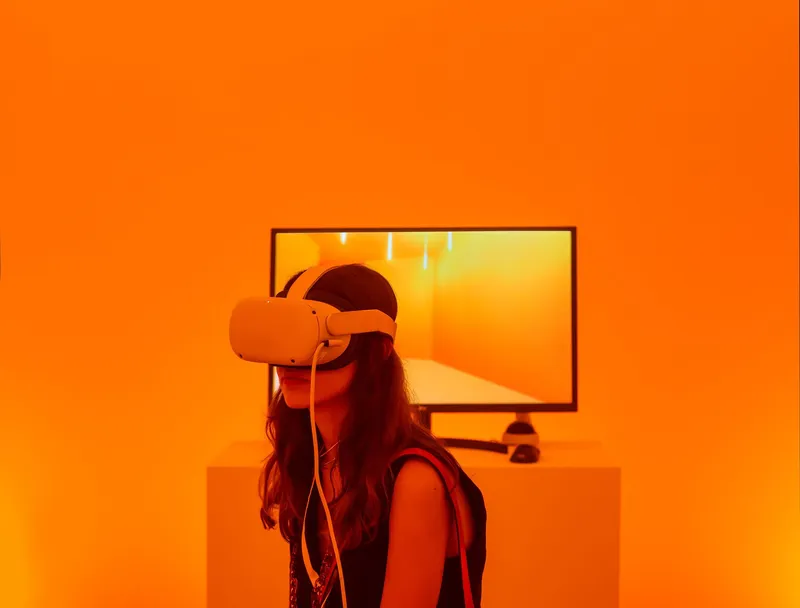 Person wearing a virtual reality headset in front of a screen in an orange-lit room