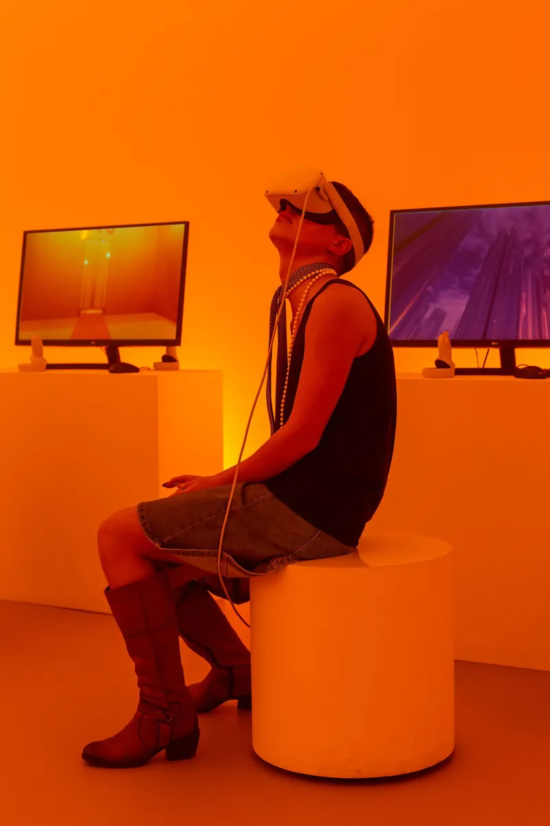 Visitor seated on cylindrical plinth wearing headphones under orange ambient lighting