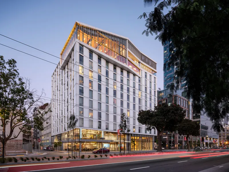 Street view of the white paneled facade with vertical fins screening the illuminated upper level at dusk