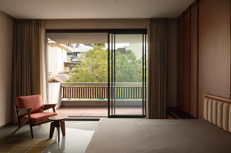 Bedroom opening to a balcony with slatted railing and treetops beyond the sliding glass doors