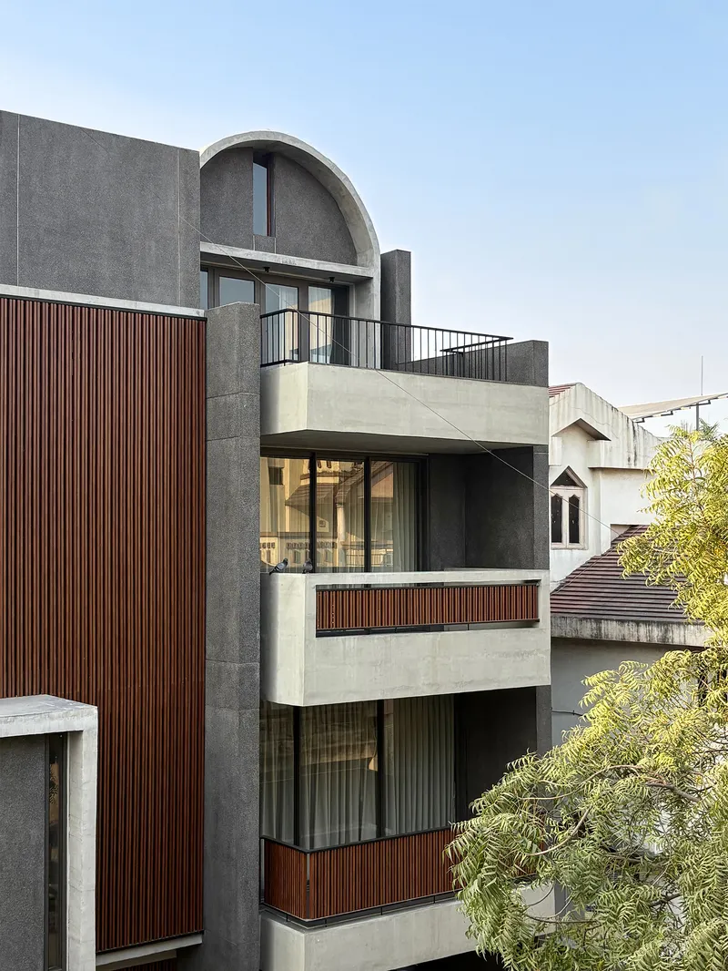 Street view of the layered concrete and timber-slatted facade with arched vault and cantilevered balconies