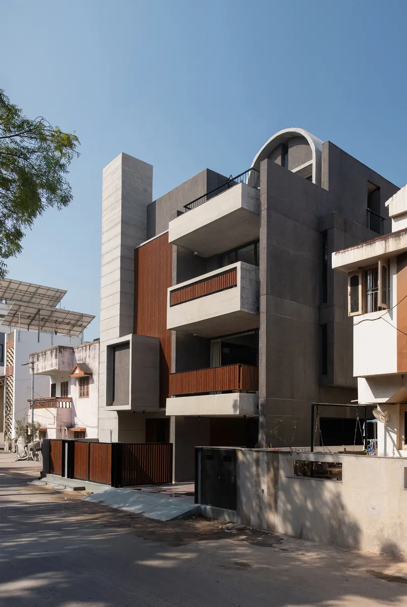 Street view of the facade with concrete volumes, timber screening, and an arched tower under a clear sky