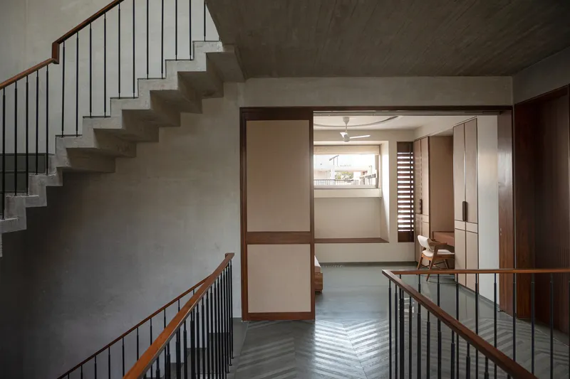 Staircase landing with timber-framed screen panels and chevron-patterned floor tile casting shadows from daylight