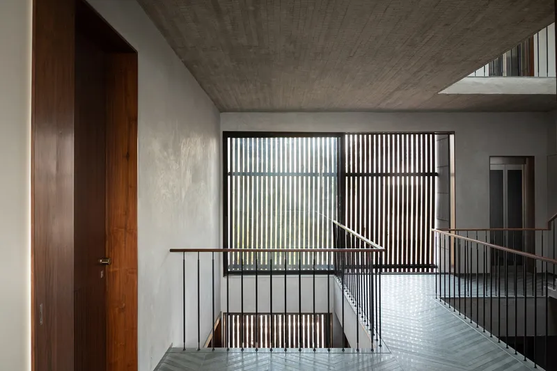 Upper landing with vertical timber slat screen filtering daylight into the stairwell with concrete ceiling