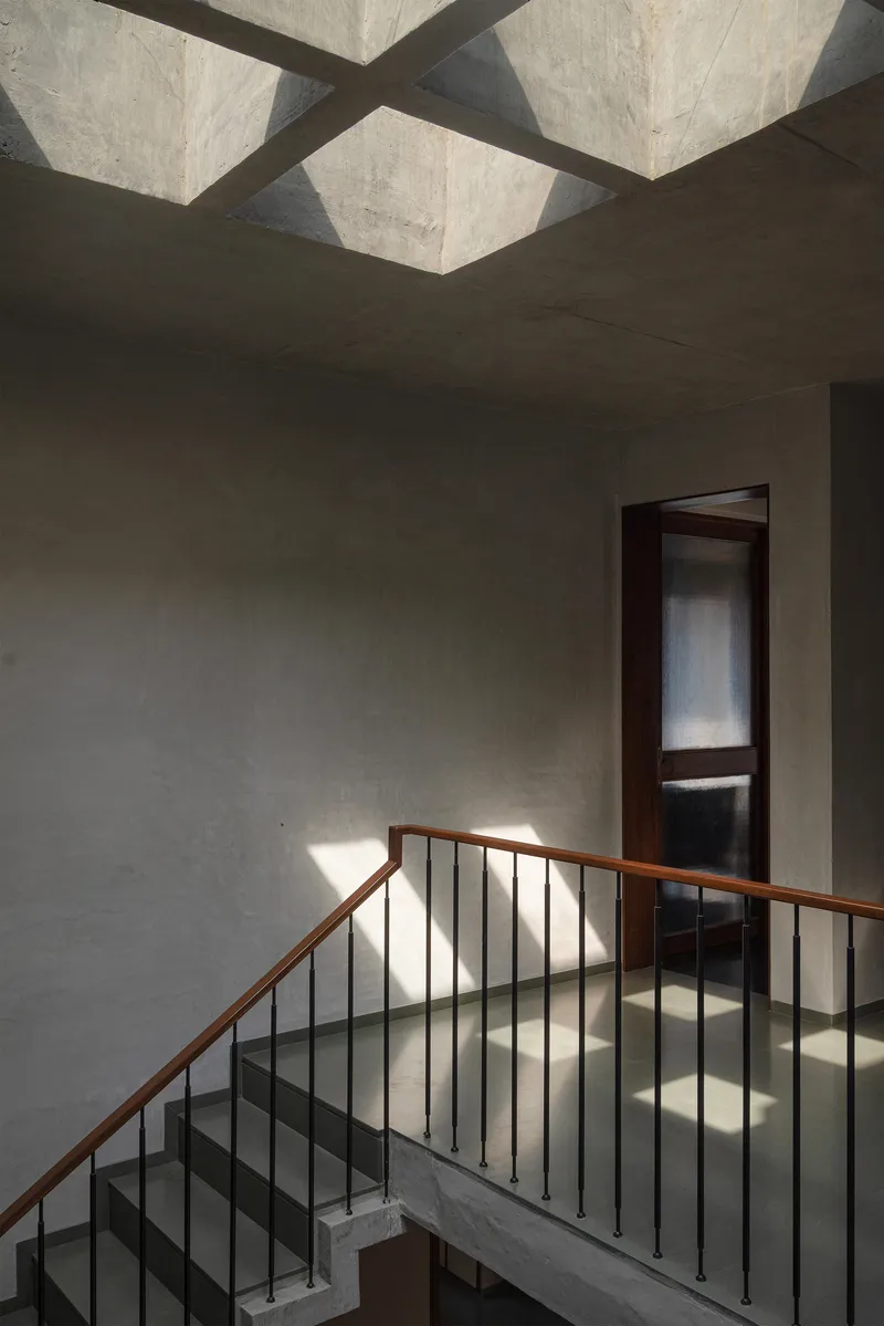 Stair railing detail with sunlight casting shadows through geometric concrete ceiling coffers above
