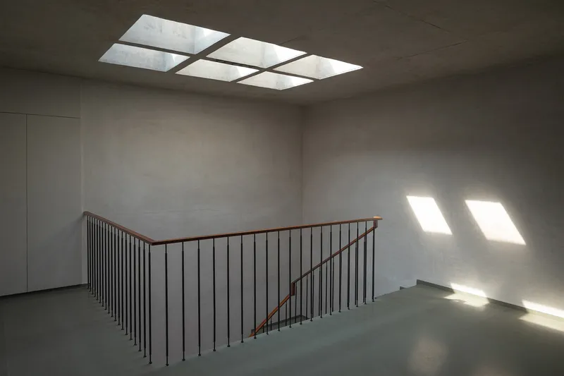 Stairwell landing with grid skylight washing concrete walls and floor with natural light