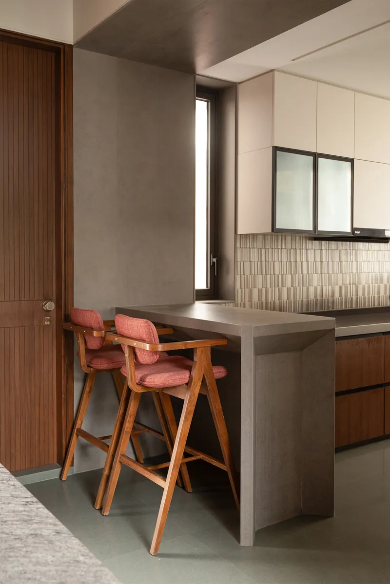 Kitchen counter with pink upholstered bar stools beside a narrow vertical window and tiled backsplash