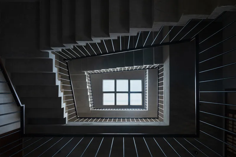 Upward view of rectangular stairwell with dark timber treads spiraling around a central skylight