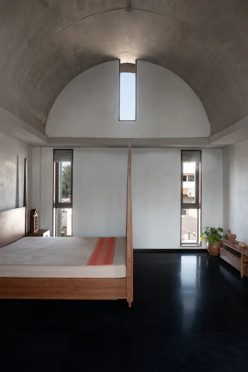 Bedroom beneath a concrete barrel vault with a vertical slot skylight at the apex