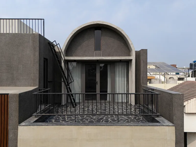 Exterior view of arched rooftop volume with mosaic terrace and black metal railings overlooking adjacent buildings