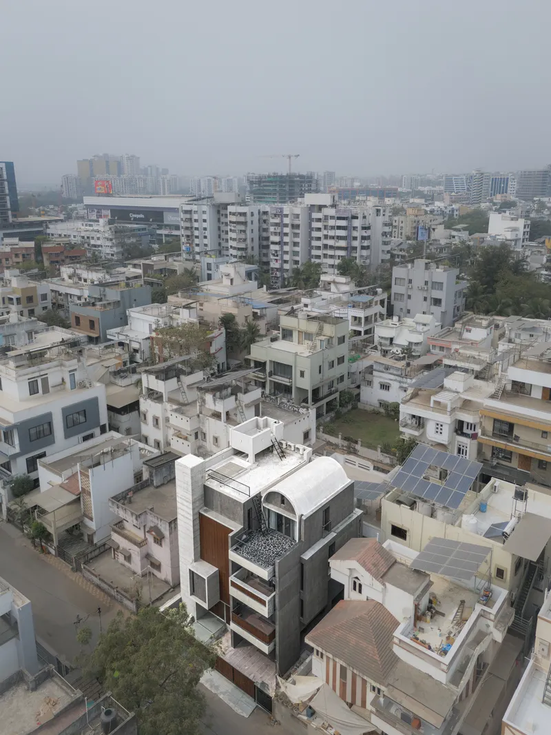 Aerial view of the multi-storey residence with curved roof volumes surrounded by dense urban fabric under overcast skies