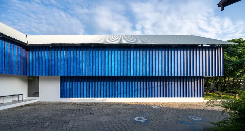 Long blue corrugated facade with horizontal banding and metal roof edge against cloudy sky