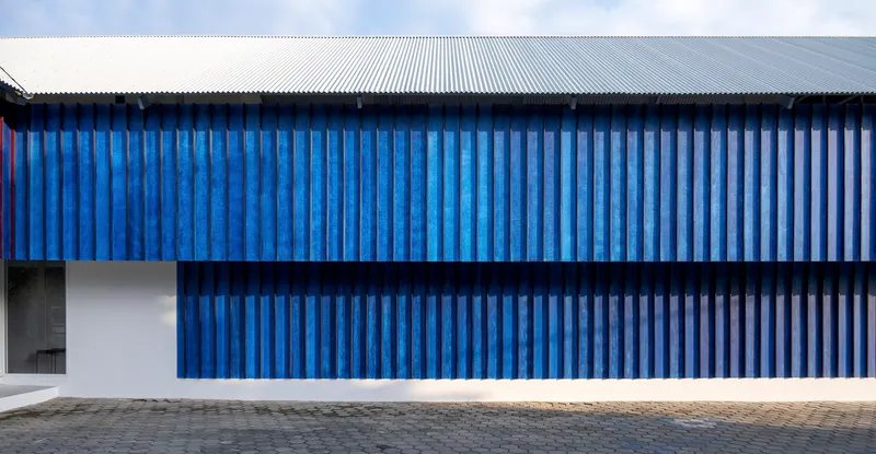 Street facade with vertical blue corrugated metal panels above a white base and corrugated metal roof