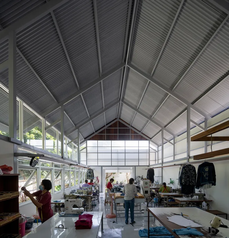 Workshop floor with sewing stations and workers under the steel-framed gabled ceiling with corrugated cladding