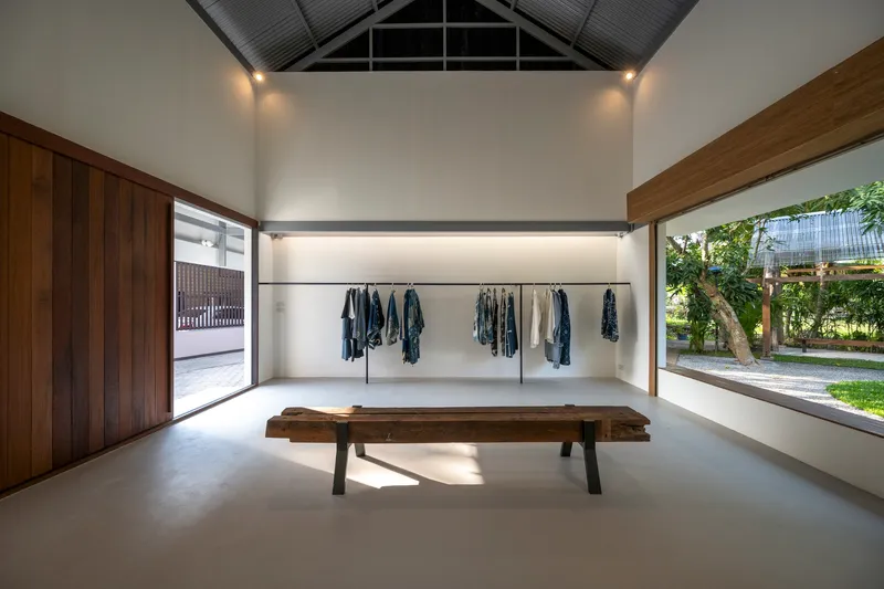 Retail space with timber bench, hanging garments, and horizontal windows framing the garden outside