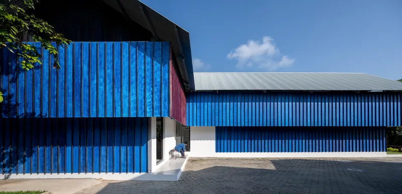 Street view of the blue corrugated metal facade with recessed entrance under partly cloudy skies