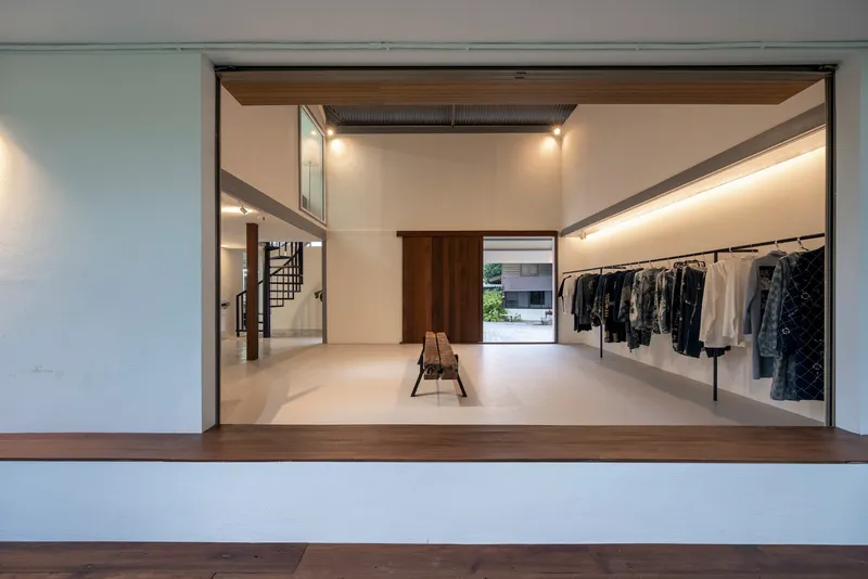 View through wide timber-framed opening showing the studio interior with clothing racks and spiral stair