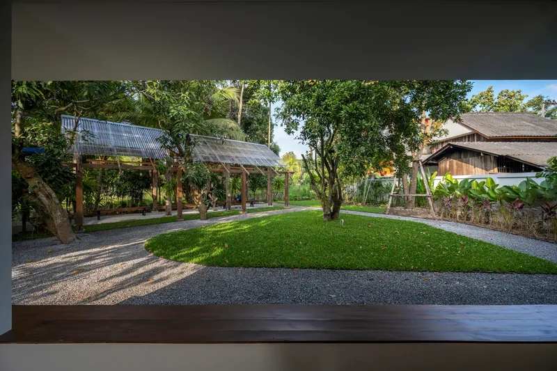 Framed view from interior to the garden courtyard with lawn, gravel paths, and timber pavilion structures