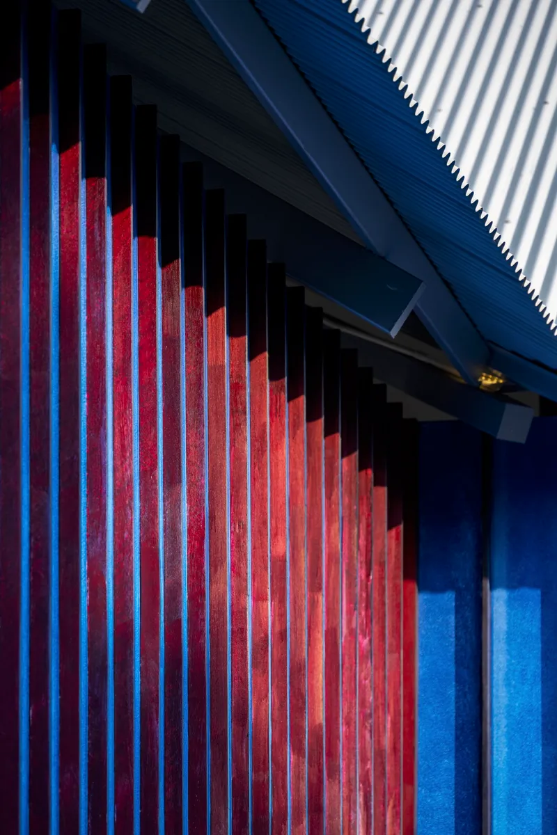 Red vertical timber slats against a corrugated metal soffit at dusk