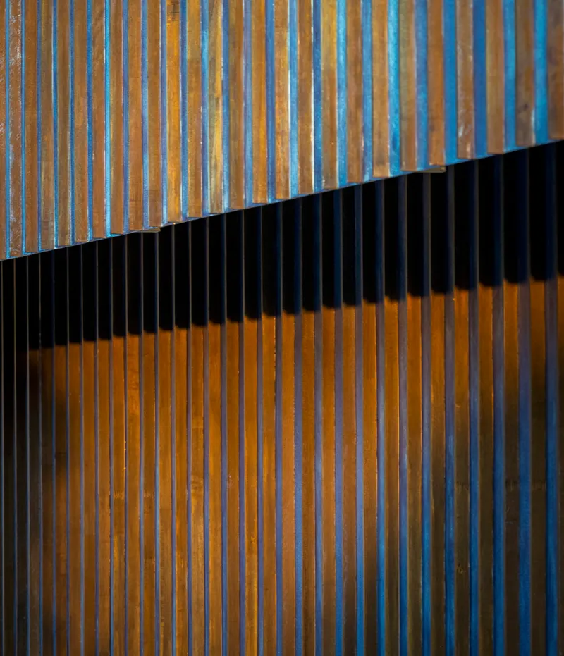 Diagonal metal screen casting shadows across vertical timber slats in afternoon light