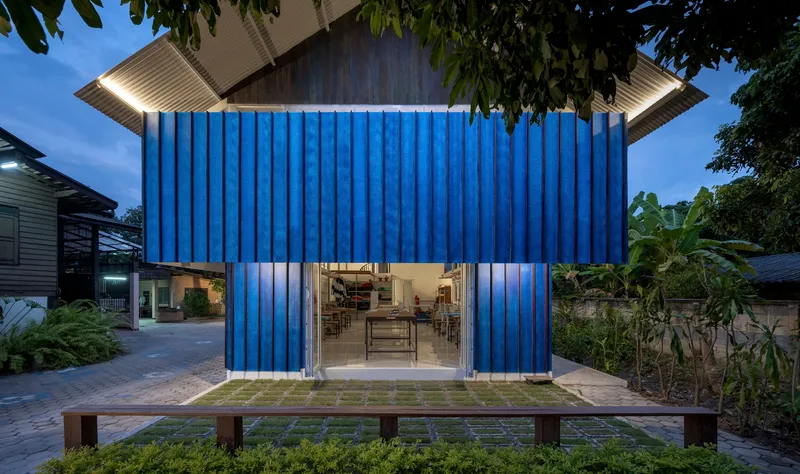 Blue corrugated facade with central glazed opening and timber bench at dusk