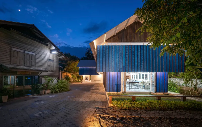 Illuminated pavilion with ribbed blue walls and upswept roof under evening sky