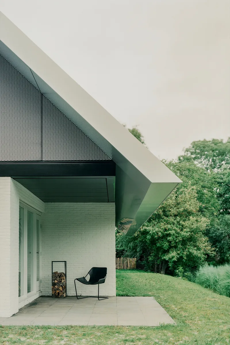 Covered terrace with perforated metal soffit and white brick wall overlooking lawn