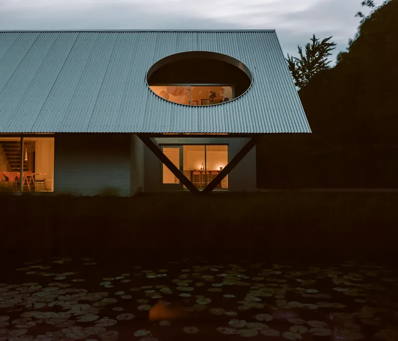 Facade with circular roof opening and angled steel brace illuminated at dusk