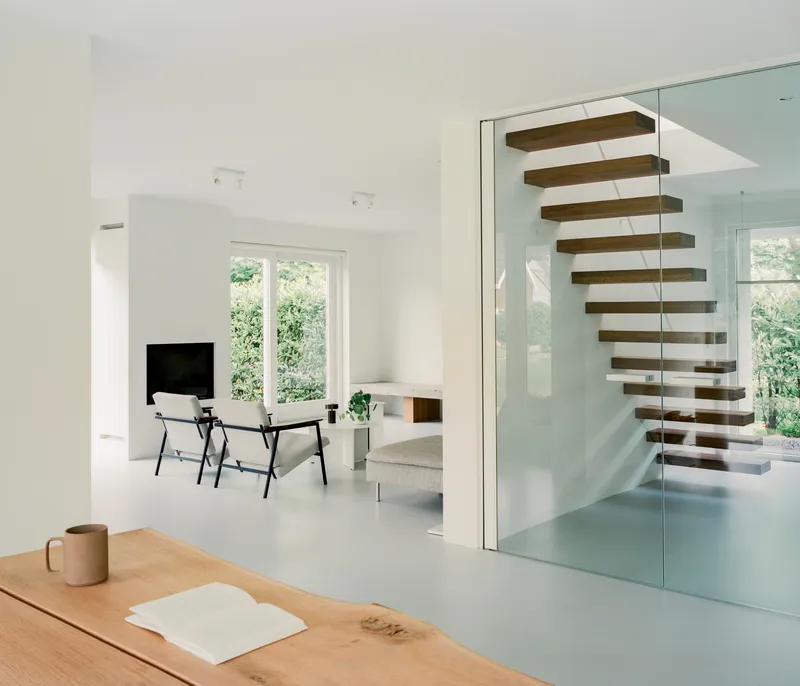 Open-plan interior with floating timber staircase behind glass partition and garden view beyond