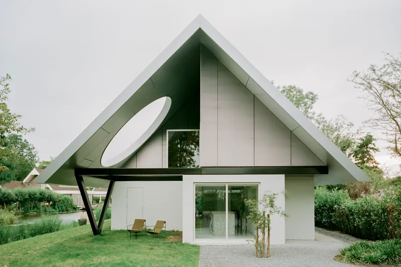 Gabled corrugated metal roof with oval window and cantilevered steel brace under overcast sky