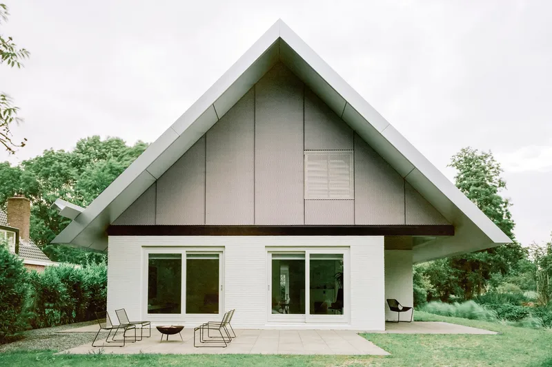Rear terrace with sliding glass doors beneath the pitched metal roof and landscaped surroundings