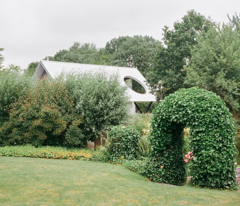View through mature garden showing the corrugated roof and circular window beyond ivy-covered walls