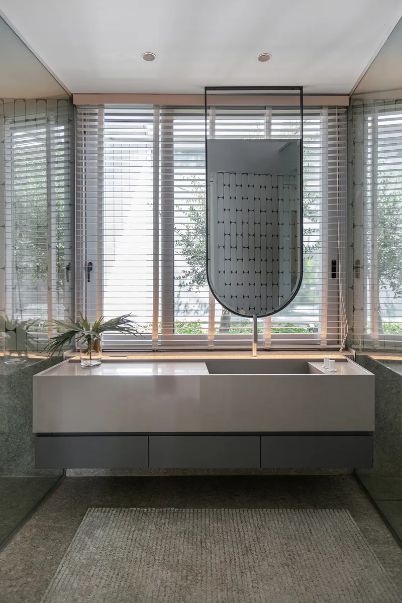 Freestanding white bathtub beneath a suspended screen and full-height louvered windows overlooking garden plantings