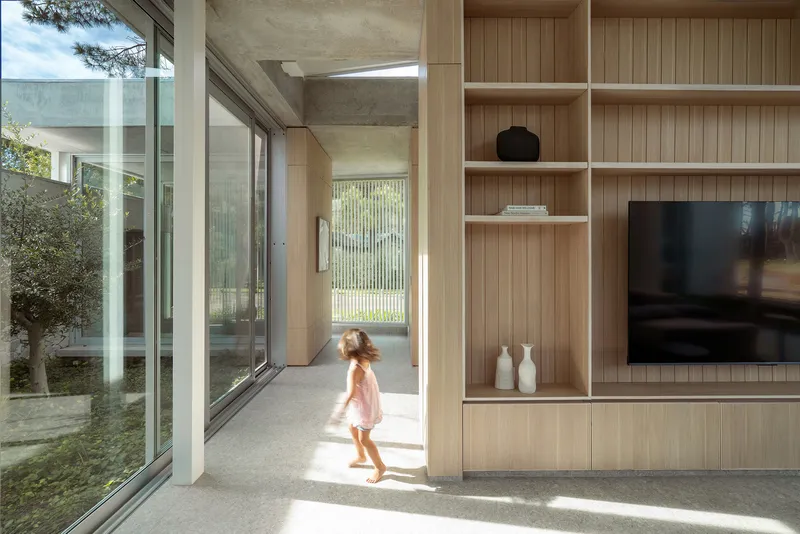 Interior corridor with timber shelving and a child walking toward glazed courtyard opening