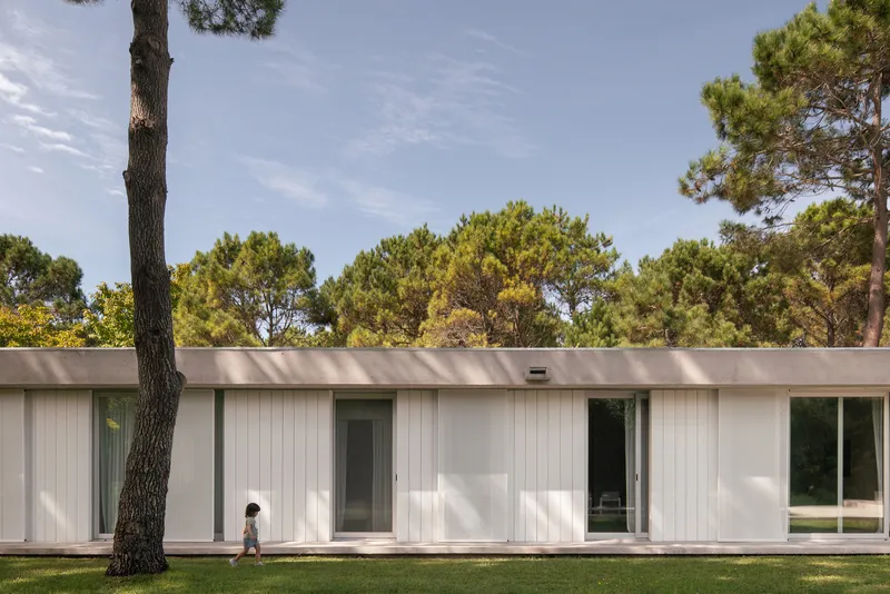 Linear facade with vertical white panels and a child walking across the lawn